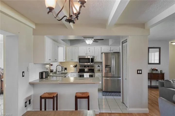 Kitchen with backsplash, appliances with stainless steel finishes, a peninsula, white cabinets, and a sink