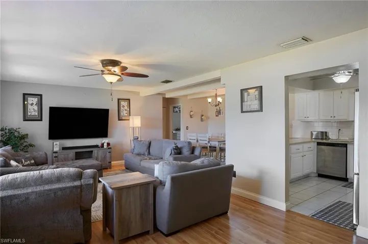Living area featuring light wood-style flooring, ceiling fan with notable chandelier, and visible vents