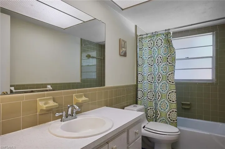 Full bathroom with tile walls, toilet, vanity, and shower / tub combo