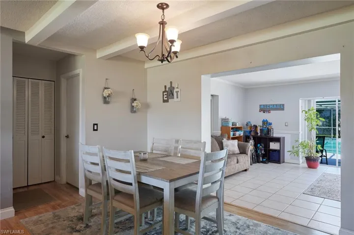Dining space featuring beamed ceiling, light wood-style flooring, a chandelier, and a textured ceiling