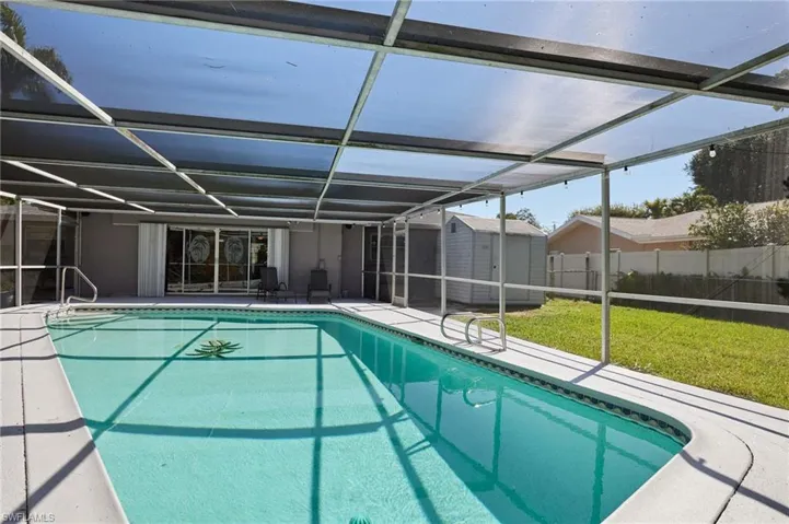 View of swimming pool with fence, an outdoor structure, a storage shed, a patio area, and a lanai
