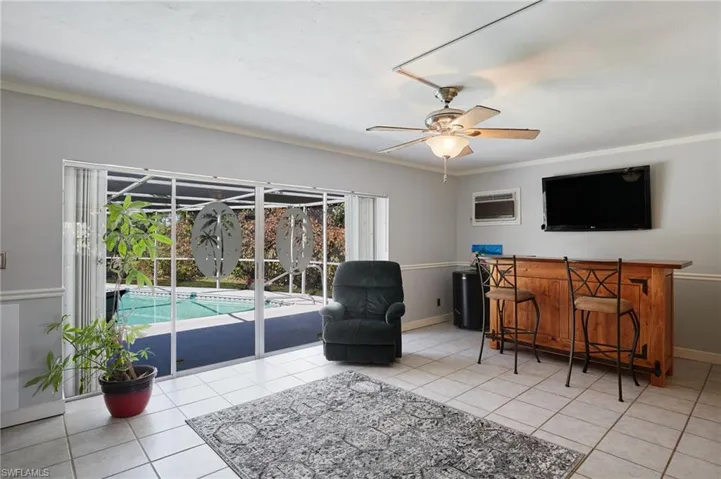 Tiled living room featuring crown molding, baseboards, a bar, a wall mounted AC, and a ceiling fan