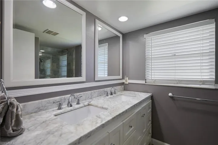 Full bath with a sink, visible vents, tiled shower, and double vanity