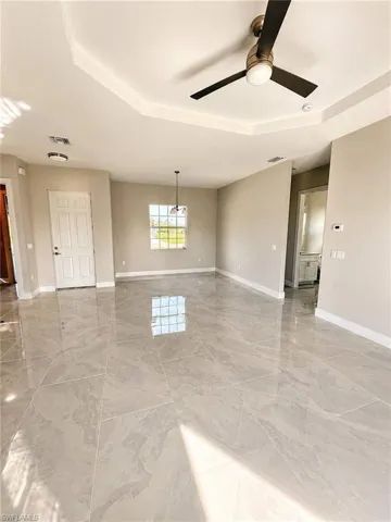 Expansive living space featuring large-format tile flooring, a tray ceiling, and a contemporary ceiling fan