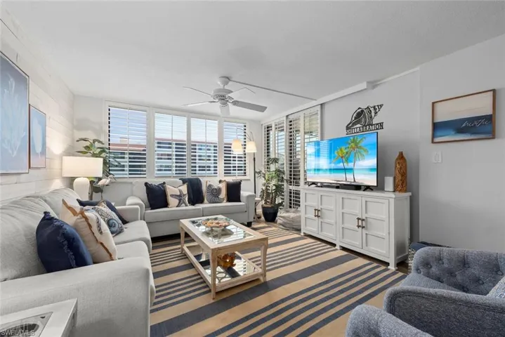 Living area featuring white paneled accent wall, expansive windows with plantation shutters, and a ceiling fan with integrated lighting