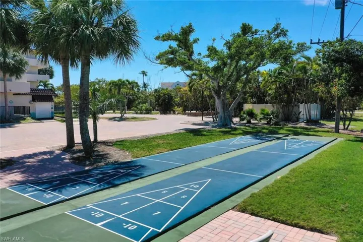 Outdoor shuffleboard courts featuring a paved surface, manicured lawn areas, mature palm trees, and brick-paver walkways