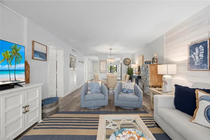 Living area featuring wood-finish flooring, white shiplap accent wall, recessed built-in shelving, and a tiered drum chandelier
