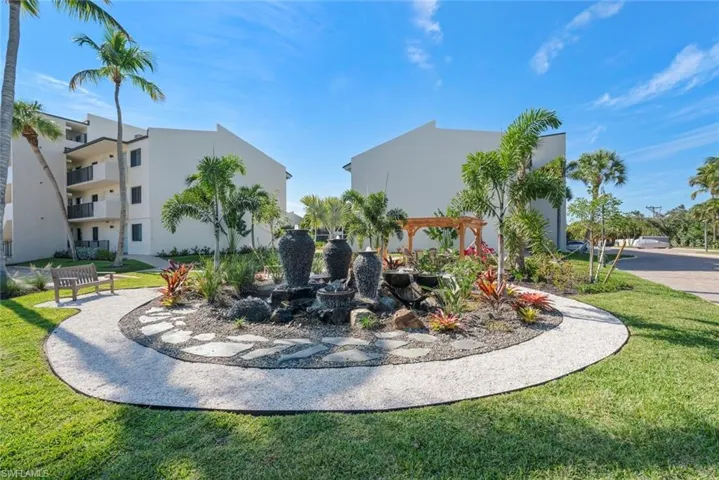 Common area courtyard featuring a triple-tier stone fountain, flagstone hardscaping, manicured lawn, palm trees, and a wooden pergola