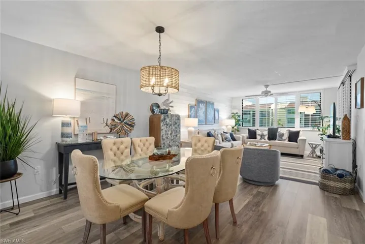 Open living area featuring wood-finish flooring, a decorative shiplap accent wall, a woven drum-style chandelier, and large windows with integrated blinds