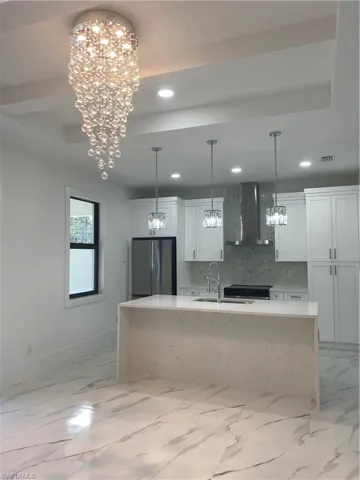 Kitchen with sink, refrigerator, an island with sink, range hood, and white cabinets