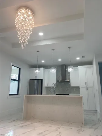 Kitchen with extractor fan, tasteful backsplash, white cabinets, fridge, and an inviting chandelier