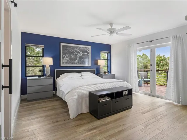 Primary bedroom featuring access large balcony, custom wood flooring, multiple windows, and a ceiling fan