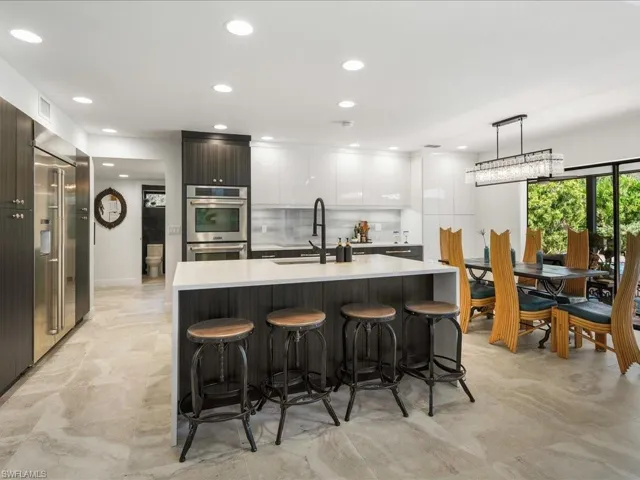 Kitchen with modern cabinets, a sink, double oven, an eat-in island bar, and light countertops