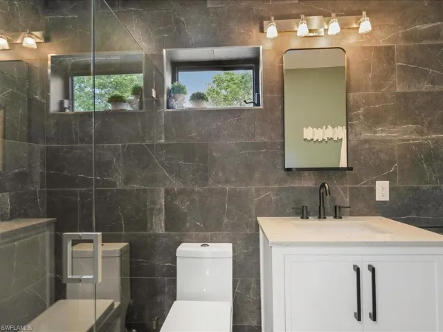 Bathroom with tile walls, plenty of natural light, toilet, and vanity