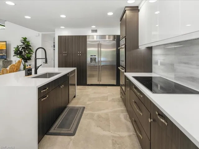 Kitchen with appliances with stainless steel finishes, a sink, light countertops, dark brown cabinetry, and a kitchen island with sink