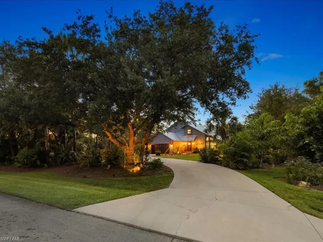 View of property hidden behind natural elements with curved driveway and a front lawn