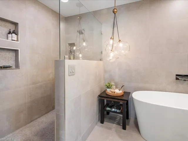 Primary bathroom with a walk in shower, tile walls, a deep soaking tub, and custom light fixtures
