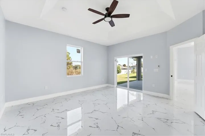 Spare room with a tray ceiling, ceiling fan, and light marble finish floors