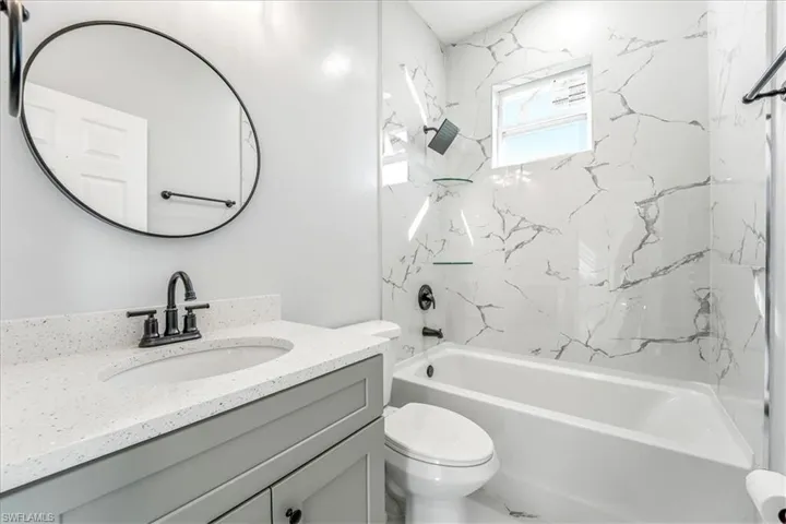 Full bath with a combined bath / shower with marble appearance and vanity