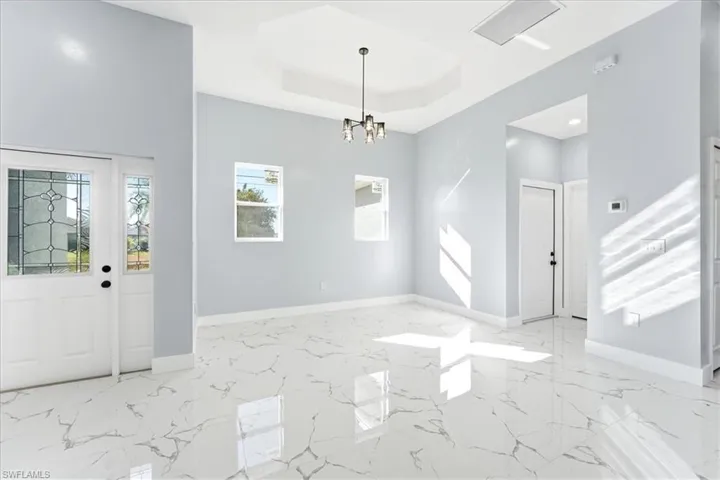 Entrance foyer featuring a raised ceiling, a chandelier, and light marble finish flooring