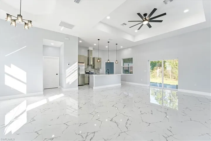 Unfurnished living room featuring a tray ceiling, ceiling fan, recessed lighting, light marble finish flooring, and a chandelier