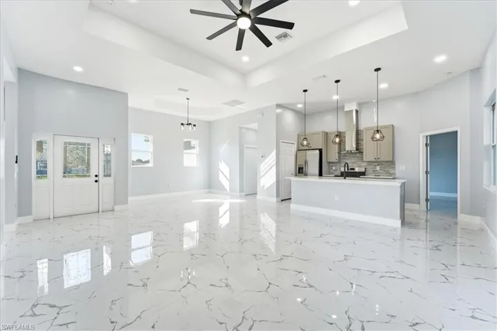 Unfurnished living room featuring a tray ceiling, recessed lighting, ceiling fan, a chandelier, and a high ceiling