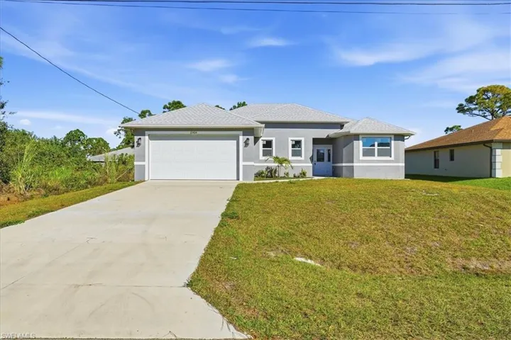 Prairie-style home featuring concrete driveway, stucco siding, a front lawn, and a garage