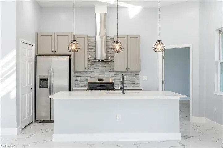 Kitchen with a high ceiling, stainless steel appliances, pendant lighting, light stone counters, and backsplash