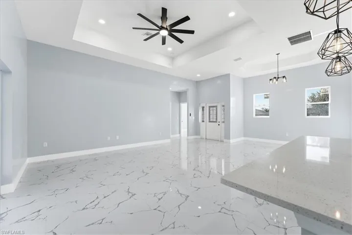 Unfurnished living room featuring a tray ceiling, light marble finish floors, recessed lighting, a ceiling fan, and a chandelier