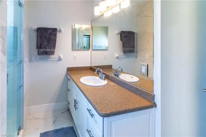 Bathroom featuring vanity, light marble finish floors, and a marble finish shower