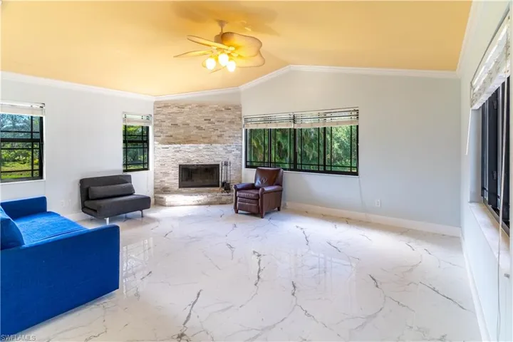 Living room with a large fireplace, crown molding, ceiling fan, and light marble finish flooring