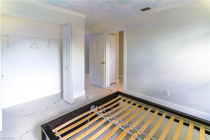 Unfurnished bedroom featuring light marble finish floors, crown molding, and a closet