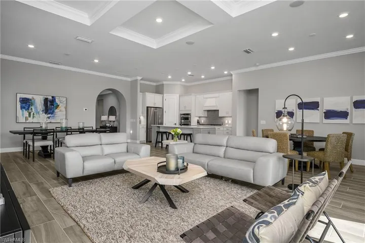 Open living room, dining room, kitchen, and kitchen cafe. Note the crown molding throughout, coffered tray ceilings, and tile flooring throughout the home.