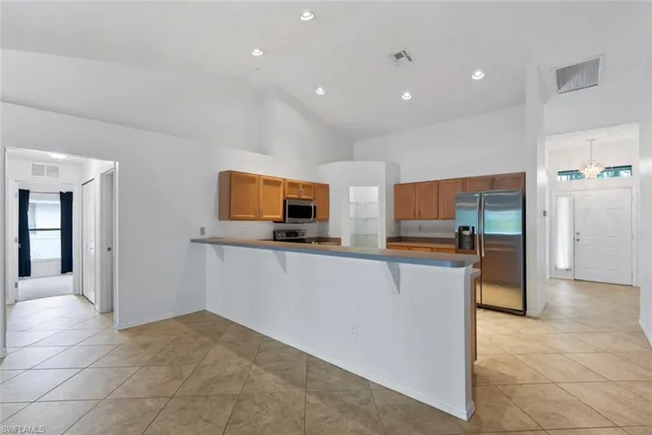 Kitchen featuring visible vents, appliances with stainless steel finishes, high vaulted ceiling, a peninsula, and a breakfast bar