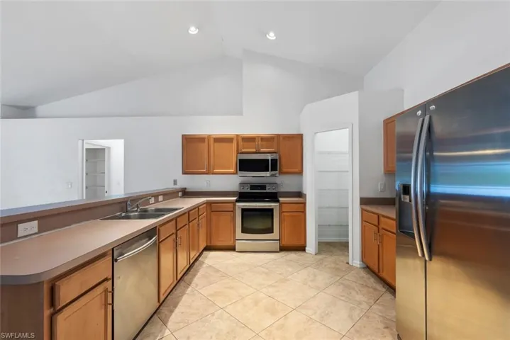 Kitchen featuring a sink, high vaulted ceiling, light tile patterned floors, a peninsula, and stainless steel appliances