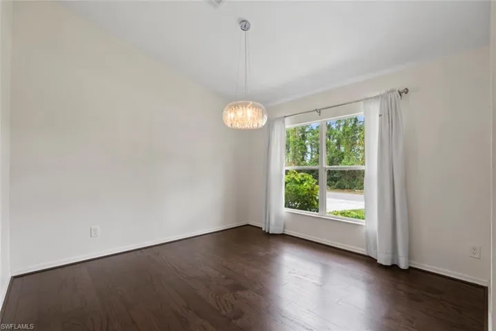 Spare room featuring a chandelier, baseboards, and dark wood finished floors