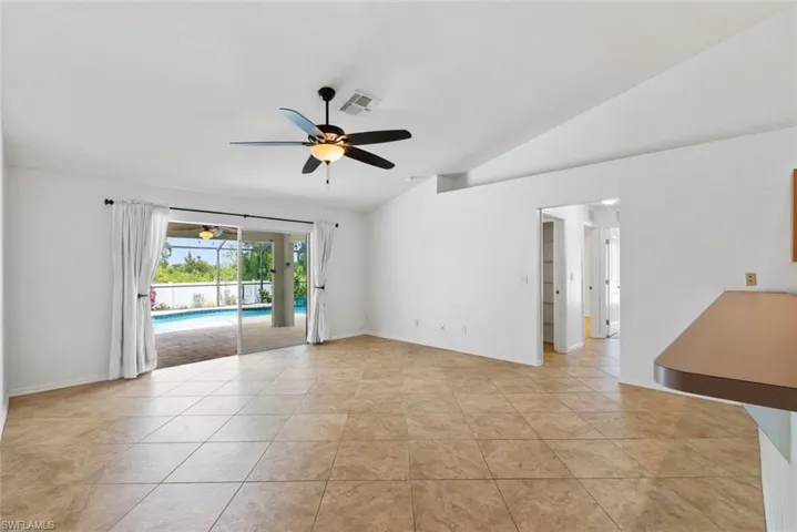 Empty room featuring visible vents, baseboards, ceiling fan, light tile patterned floors, and vaulted ceiling