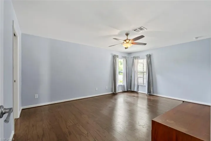 Empty room featuring ceiling fan, visible vents, dark wood-style floors, and baseboards