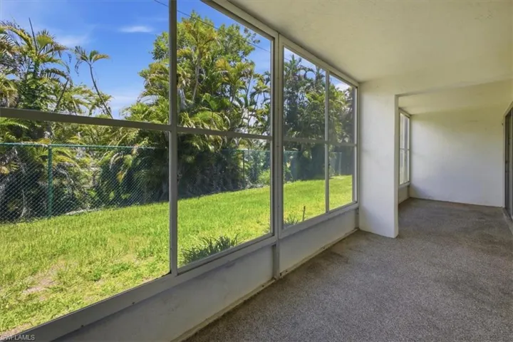Screened patio featuring a textured floor, white walls, and clear views of a green lawn and mature palm trees