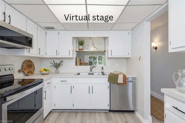 Kitchen featuring white cabinetry, light-toned countertops, a stainless steel over-the-range microwave, a stainless steel dishwasher, and wood-finish flooring