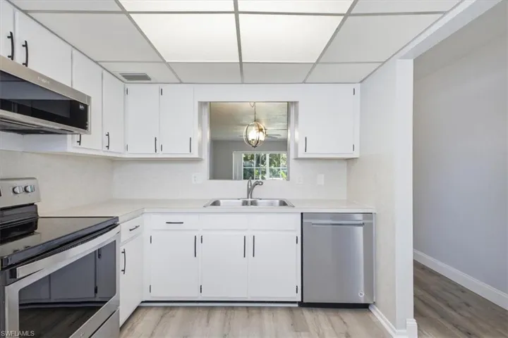 Kitchen featuring white cabinetry with black hardware, stainless steel appliances, a double basin sink, and wood-finish flooring