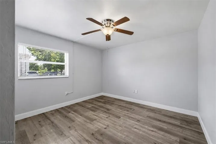 Spacious room featuring wood-finish flooring, light grey painted walls, white baseboards, and a ceiling fan with integrated lighting