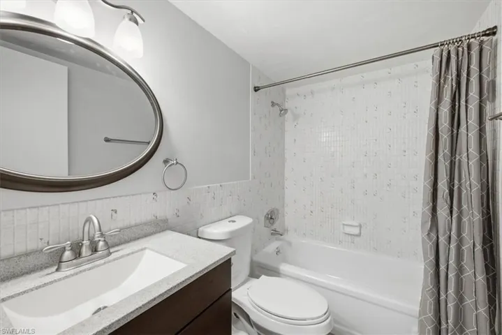 Bathroom featuring a dark wood-finish vanity with a light speckled countertop, an oval mirror, and a full-size bathtub with a tiled surround
