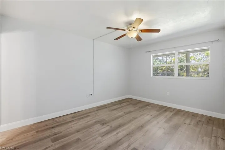 Room featuring wood-finish flooring, white baseboards, and a ceiling fan with light fixture