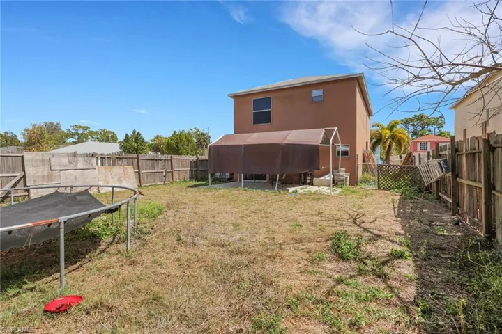 Rear view of house with a trampoline, a fenced backyard, and stucco siding
