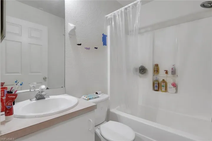 Full bathroom with a textured wall, vanity, and shower / bathtub combination with curtain