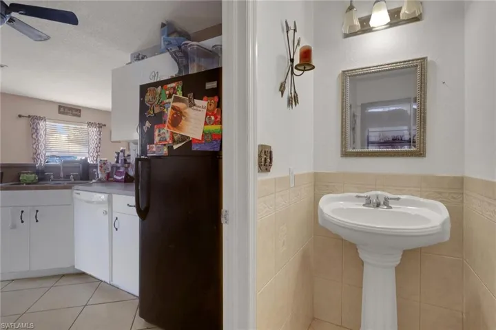 Bathroom with tile walls, wainscoting, ceiling fan, light tile patterned floors, and vanity