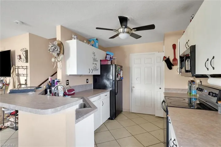 Kitchen with black appliances, white cabinets, a peninsula, light tile patterned flooring, and a textured ceiling
