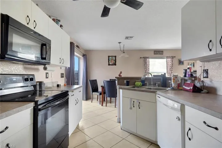 Kitchen with black appliances, a peninsula, white cabinetry, light tile patterned floors, and a textured ceiling