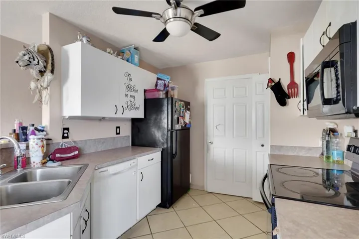 Kitchen featuring black appliances, light countertops, white cabinetry, a ceiling fan, and light tile patterned floors